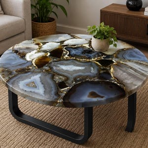 May include: A round coffee table featuring a tabletop composed of polished, multi-colored agate slices in shades of blue, gray, white, and brown. The table is supported by a black metal frame with curved legs and includes the text StoniracraftsIndia.
