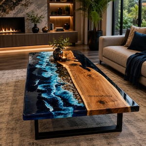 Op de afbeelding: Een rechthoekige salontafel met een houten blad met natuurlijke rand aan de ene kant en een glanzend blauw harsgedeelte aan de andere kant, dat oceaangolven met ingebedde kiezels nabootst. De tafel heeft een zwart metalen frame en de tekst StoniracraftsIndia.