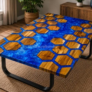 May include: A rectangular coffee table featuring a tabletop made of natural wood hexagons embedded in a vibrant, swirling blue resin river design. The table is supported by a black metal frame with U-shaped legs and displays the text StoniracraftsIndia.