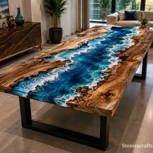 Puede incluir: Una mesa de comedor rectangular con un tablero de madera de borde natural y una incrustación central de resina azul. La resina imita agua corriente con detalles de espuma blanca. La mesa se apoya en patas de metal negro y muestra el texto StoniracraftsIndia.