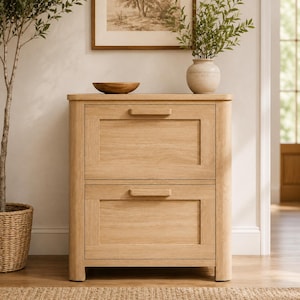May include: A light-colored wooden cabinet with two drawers. The cabinet has a rectangular shape with a natural wood grain finish. The drawers have simple, horizontal handles. A wooden bowl and a vase with greenery sit on top.