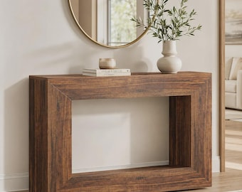 May include: A rectangular console table with a dark brown wood grain finish and a hollow center. On top sits a stack of books with the text "LIVE BEAUTIFULLY" visible on the spine, a small cylindrical container, and a white vase with green foliage.