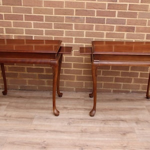 May include: A pair of matching rectangular wooden side tables with a polished dark brown finish. Each table features a smooth flat top, four slender curved legs with carved feet, and two small pull-out side extensions on the left and right sides.