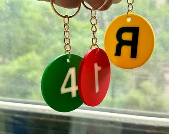 May include: Three keychains with gold-colored rings and chains. Each keychain has a circular charm in different colors: green with the number "4", red with the number "1", and yellow with the letter "Я".