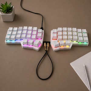 May include: A white split ergonomic mechanical keyboard with RGB backlighting. The two halves are connected by a black cable with gold-colored connectors. The keys are blank, and the device features a contoured layout for typing comfort.