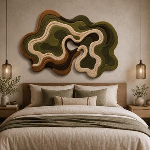 May include: A large, irregular, abstract wall hanging featuring layered, tufted textures in shades of olive green, dark brown, tan, and cream. The piece has a fluid, organic shape with concentric, wavy lines that create a sense of depth and movement.