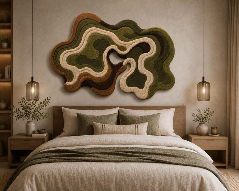 May include: A large, irregular, abstract wall hanging featuring layered, tufted textures in shades of olive green, dark brown, tan, and cream. The piece has a fluid, organic shape with concentric, wavy lines that create a sense of depth and movement.