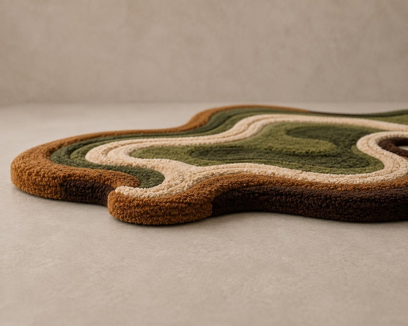 May include: An irregularly shaped tufted rug featuring a series of concentric, wavy bands in shades of dark brown, rust orange, cream, olive green, and forest green. The rug has a thick, textured pile surface with organic, flowing contours.