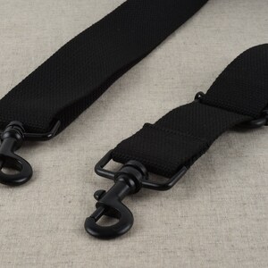 May include: Two black adjustable straps with metal clasps. The straps are made of a woven fabric.
