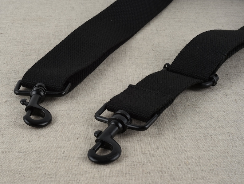 May include: Two black adjustable straps with metal clasps. The straps are made of a woven fabric.