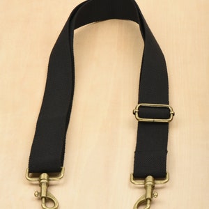May include: Black canvas shoulder strap with gold metal hardware, including two hooks and a rectangular buckle.