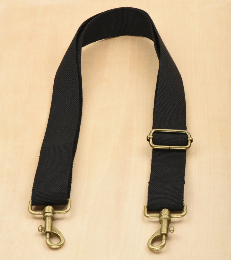 May include: Black canvas shoulder strap with gold metal hardware, including two hooks and a rectangular buckle.