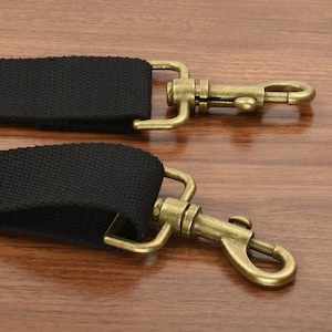 May include: Two black canvas straps with antique gold metal clasps. The clasps have a hook and loop design.