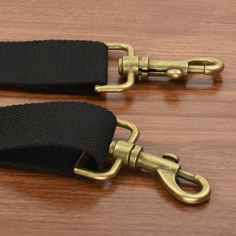 May include: Two black canvas straps with antique gold metal clasps. The clasps have a hook and loop design.