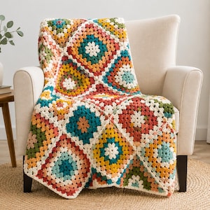 Può includere: Una colorata coperta all'uncinetto fatta a mano, drappeggiata su una poltrona color crema. La coperta presenta un design patchwork con quadrati nei toni del verde acqua, rosso, giallo e verde. La coperta è realizzata in morbido filato e presenta un motivo floreale al centro di ogni quadrato.
