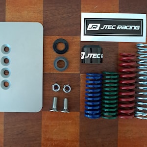 Può includere: Un assortimento di ricambi auto, tra cui una piastra argentata con quattro fori, molle rosse, blu, verdi e argentate e un adesivo bianco e nero "JTEC RACING". Sono inclusi anche anelli di gomma neri, dadi e bulloni.