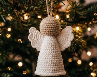 May include: A crocheted angel ornament featuring a round beige head and a white cone-shaped body. The figure has two scalloped white wings attached to the sides and a thin jute string loop at the top for hanging on a tree branch.