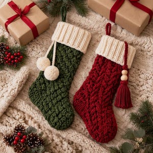 May include: Two knit Christmas stockings with cream-colored ribbed cuffs. One stocking is dark green with a textured stitch and two cream pom-poms. The other is deep red with a cable knit pattern and a matching red tassel with wooden beads.