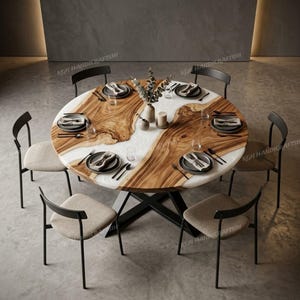 Puede incluir: Una mesa de comedor redonda con superficie de madera natural e incrustación central de resina blanca, apoyada sobre una base de metal negro en forma de X. La mesa está rodeada por seis sillas con estructura de metal negro y asientos beige.
