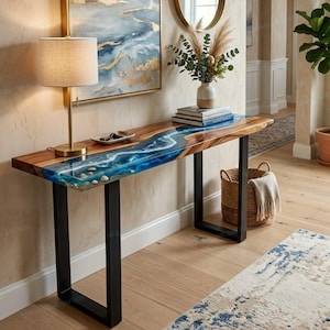 May include: A rectangular console table featuring a natural wood slab top with a central blue resin river inlay that mimics flowing water, complete with white foam details and embedded stones, supported by two black metal U-shaped legs.