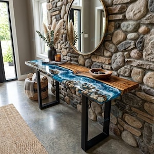 May include: A rectangular console table featuring a natural wood slab with a blue resin river inlay containing embedded river stones. The table is supported by two black metal U-shaped legs and sits against a textured stone wall with a round mirror.