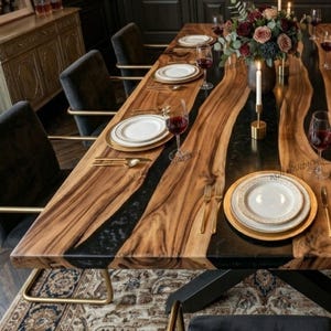 May include: A wooden dining table with a live edge design. The table has a black epoxy river running through the centre. It is set with white plates, gold cutlery, and wine glasses. A floral arrangement and candles are placed on the table. The table is approximately 200 cm long.