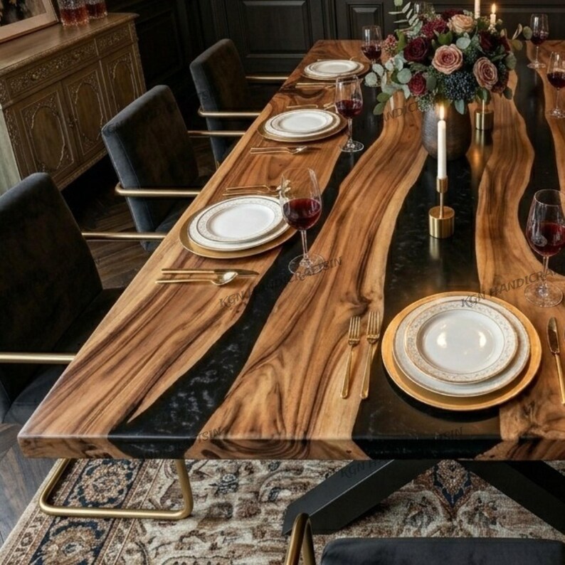 May include: A wooden dining table with a live edge design. The table has a black epoxy river running through the centre. It is set with white plates, gold cutlery, and wine glasses. A floral arrangement and candles are placed on the table. The table is approximately 200 cm long.