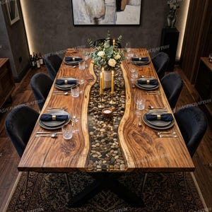 Peut inclure: Une table à manger rectangulaire en bois à bord naturel avec un canal central recouvert de verre rempli de galets de rivière lisses. La table présente une finition en grain de bois naturel, des pieds en métal noir et six chaises gris foncé.