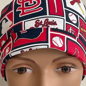 May include: Red, white, and blue baseball-themed surgical scrub hat with the St. Louis Cardinals logo and the words "St. Louis".