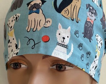 Könnte beinhalten: Eine blaue OP-Mütze mit einem Muster aus verschiedenen Hunderassen, darunter ein Mops, ein Dalmatiner, ein Terrier und ein weißer Hund. Die Mütze hat einen roten Ball und Pfotenabdrücke auf dem Stoff.