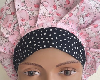 May include: A pink and white surgical scrub hat with a black and white polka dot band. The hat features a pattern of pink pigs.