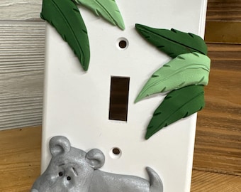 May include: A white light switch cover with a gray hippopotamus and green leaves sculpted on it.