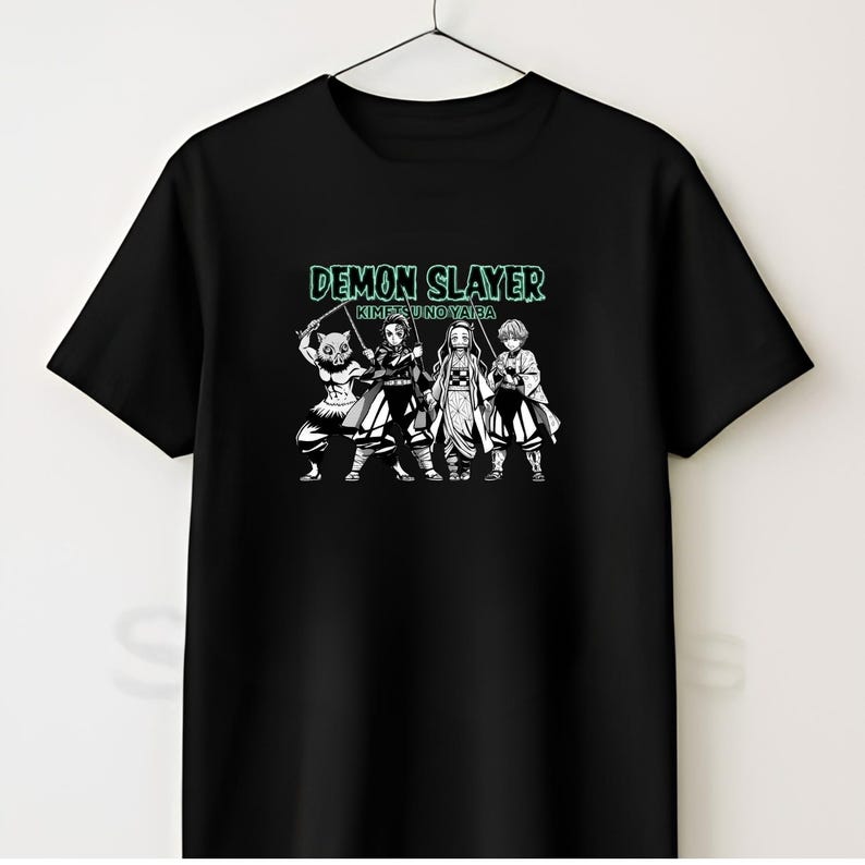 May include: A black short-sleeved t-shirt featuring a graphic print of four anime characters from Demon Slayer Kimetsu no Yaiba. The text DEMON SLAYER KIMETSU NO YAIB A is printed in a light green font above the characters, who are depicted in black and white.