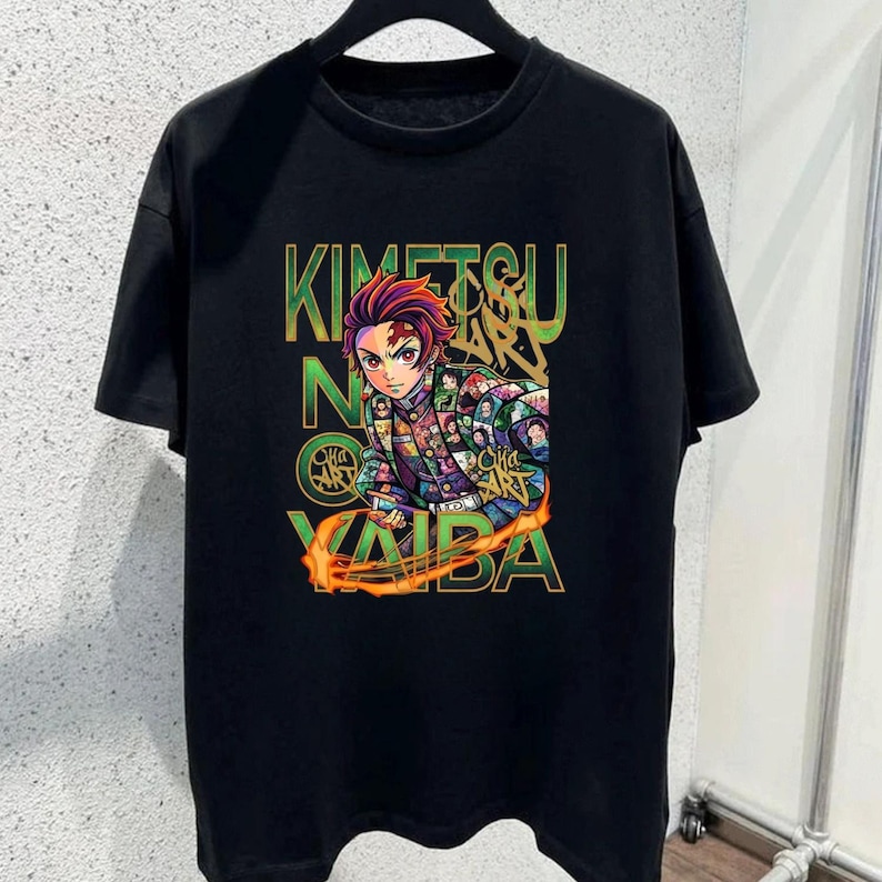May include: A black short-sleeve t-shirt featuring a graphic print of an anime character with red hair and a patterned jacket. The text KIMETSU NO YAIBA is printed in large green letters behind the character, with orange flame accents.