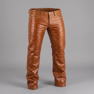 Puede incluir: Un pantalón de color tostado con un patrón de textura de piel de cocodrilo en toda la superficie. La prenda incluye una cintura estándar con trabillas para cinturón, cierre de botón frontal, cremallera y cinco bolsillos de estilo clásico.
