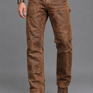 Puede incluir: Pantalones de cuero marrón con corte recto, paneles reforzados en las rodillas, remaches metálicos en las esquinas de los bolsillos, cierre de botones y una trabilla utilitaria en el lateral, combinados con botas de cuero marrón.