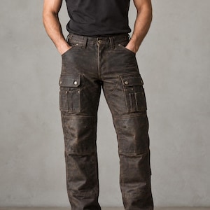 Könnte beinhalten: Dunkelbraune Leder-Cargohose mit mehreren Utility-Taschen, verstärkten Kniepartien und Knopfverschluss. Die Hose wird mit einem schlichten schwarzen T-Shirt kombiniert. Das Logo von Abdullah Leather Inc. Premium Leather Apparel ist zu sehen.