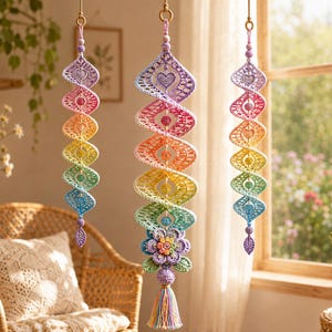 May include: Three hanging spiral ornaments crafted from crochet yarn in a rainbow gradient of purple, pink, yellow, green, and blue. Each piece features heart-shaped cutouts, small beads, and a central flower motif with a tassel at the bottom.
