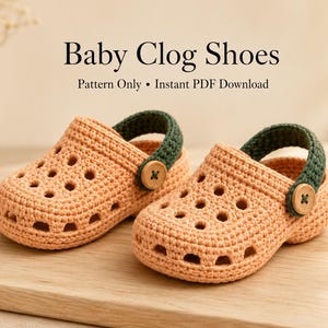 Op de afbeelding: Een paar perzikkleurige gehaakte babyklompen met donkergroene hielbandjes en lichtbruine houten knopen. De tekst Baby Clog Shoes Pattern Only Instant PDF Download is zichtbaar boven de schoenen, die voorzien zijn van ventilatiegaten.