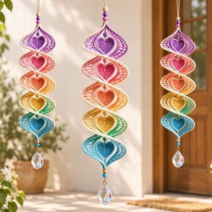 May include: Three hanging spiral ornaments featuring a gradient of crocheted hearts in purple, pink, orange, yellow, green, and blue. Each ornament is suspended by a string with wooden beads and terminates in a clear, faceted crystal prism.