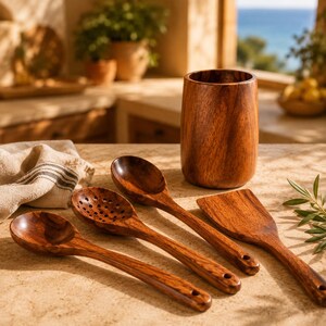 May include: A wooden kitchen utensil set including a spoon, slotted spoon, spatula, and utensil holder. The set is made of a rich, dark brown wood and is arranged on a light-colored surface. The utensils are designed for cooking and food preparation.