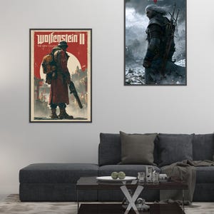 Peut inclure: Deux affiches encadr&eacute;es sur un mur blanc. L'affiche de gauche est pour "Wolfenstein II" avec une figure en manteau rouge. L'affiche de droite est pour "The Witcher 3: Wild Hunt" avec un personnage en armure. Un canap&eacute; gris fonc&eacute; et une table basse sont devant.