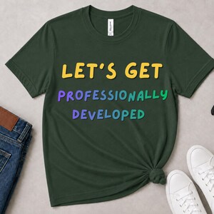 May include: A dark green short-sleeved t-shirt featuring the text LET'S GET in yellow, PROFESSIONALLY in a multi-coloured gradient, and DEVELOPED in a blue-to-green gradient. The shirt has a crew neckline and a standard fit.