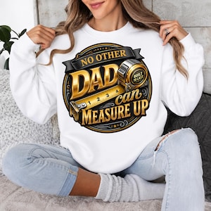 May include: A white long-sleeve sweatshirt featuring a circular graphic with gold and black text that reads NO OTHER DAD can MEASURE UP. The design includes a metallic gold tape measure illustration with the text BUILT TO LAST on its side.
