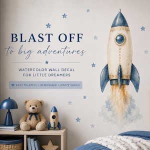 Op de afbeelding: Een aquarel muursticker met een raket met blauwe vinnen en een gele uitlaatpluim, omringd door blauwe sterren. De tekst luidt: BLAST OFF to big adventures, WATERCOLOR WALL DECAL FOR LITTLE DREAMERS, EASY TO APPLY, REMOVABLE, MATTE FINISH.