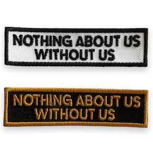 May include: Two embroidered patches with the text "Nothing About Us Without Us" in black lettering. The top patch is white with a black border. The bottom patch is black with a gold border.