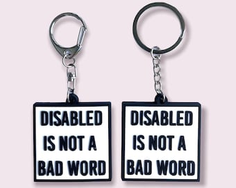 May include: Two black keychains with silver key rings. Each keychain has a white square tag with the text "DISABLED IS NOT A BAD WORD" in black.