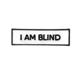Puede incluir: Parche rectangular blanco con borde negro y el texto "I AM BLIND" en negro.