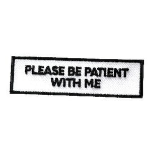 May include: White rectangular patch with black border and text that reads "PLEASE BE PATIENT WITH ME".