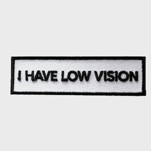 Puede incluir: Parche rectangular blanco con borde negro y el texto "I HAVE LOW VISION" en negro.